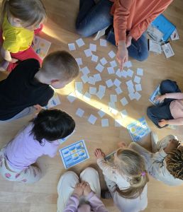 kinder sitzen im Kreis auf dem Boden, vor sich verdeckte Karten